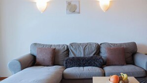 Una sala de estar moderna con un sofá modular, dos luces fijadas a la pared y un frutero sobre una mesita.
