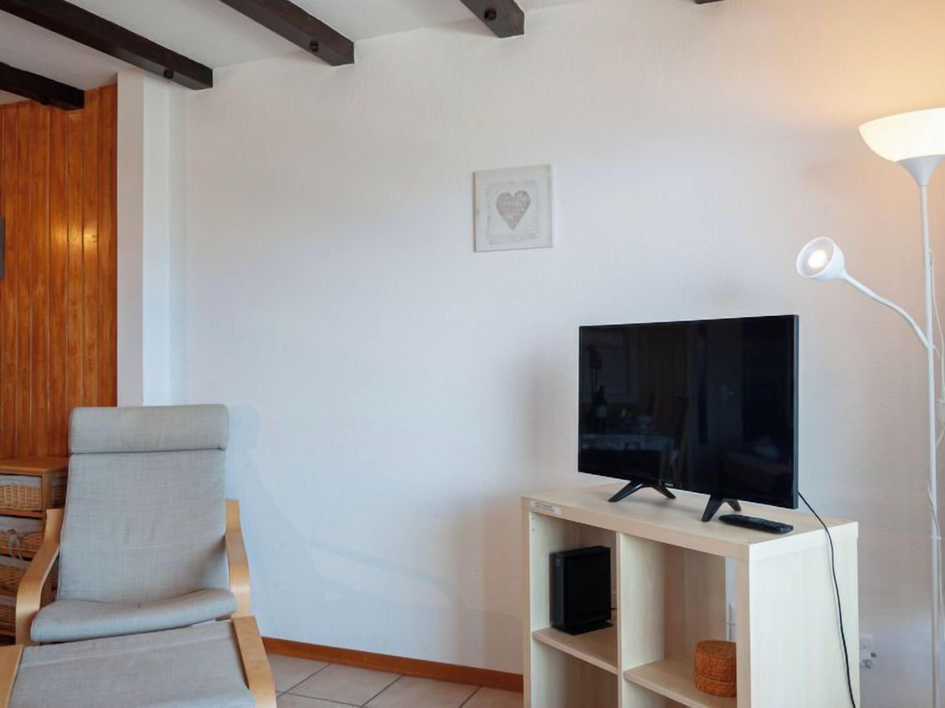Un salon avec un téléviseur à écran plat posé sur un meuble, un fauteuil, un lampadaire blanc et un panneau mural en bois.