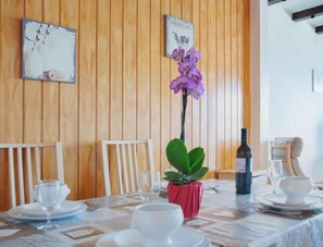 Ein Esstisch ist gedeckt mit weißen Tellern, Gläsern und einer Weinflasche. Auf dem Tisch steht eine Orchidee im Topf.