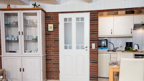 A kitchen with white cabinets, a microwave, and a dining area with a table and chairs. - Klaffmuschel by Interhome (Norddeich)