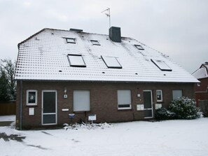 Ein zweistöckiges Backsteinhäuschen mit schneebedecktem Dach, Schornstein und kleiner angebauter Garage.