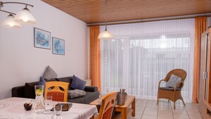 Ein Essbereich mit Tisch für zwei Personen, einem Korbstuhl und einer Couch mit Kissen.