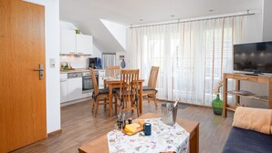 Een moderne woonkamer met een eetgedeelte, houten meubels, een televisie en een keuken op de achtergrond.