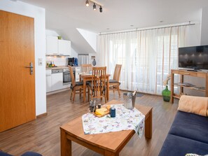 A modern living room with a dining area, wooden furniture, a television, and a kitchen in the background. - Ballertutje by Interhome (Norddeich)