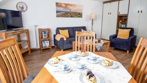 Een gezellige woonkamer met een eettafel gedekt voor een maaltijd, een bank, een televisie en een boekenkast.