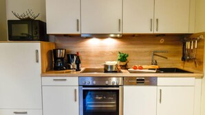 Une cuisine compacte avec des meubles blancs, un four à micro-ondes, une machine à café et un évier.