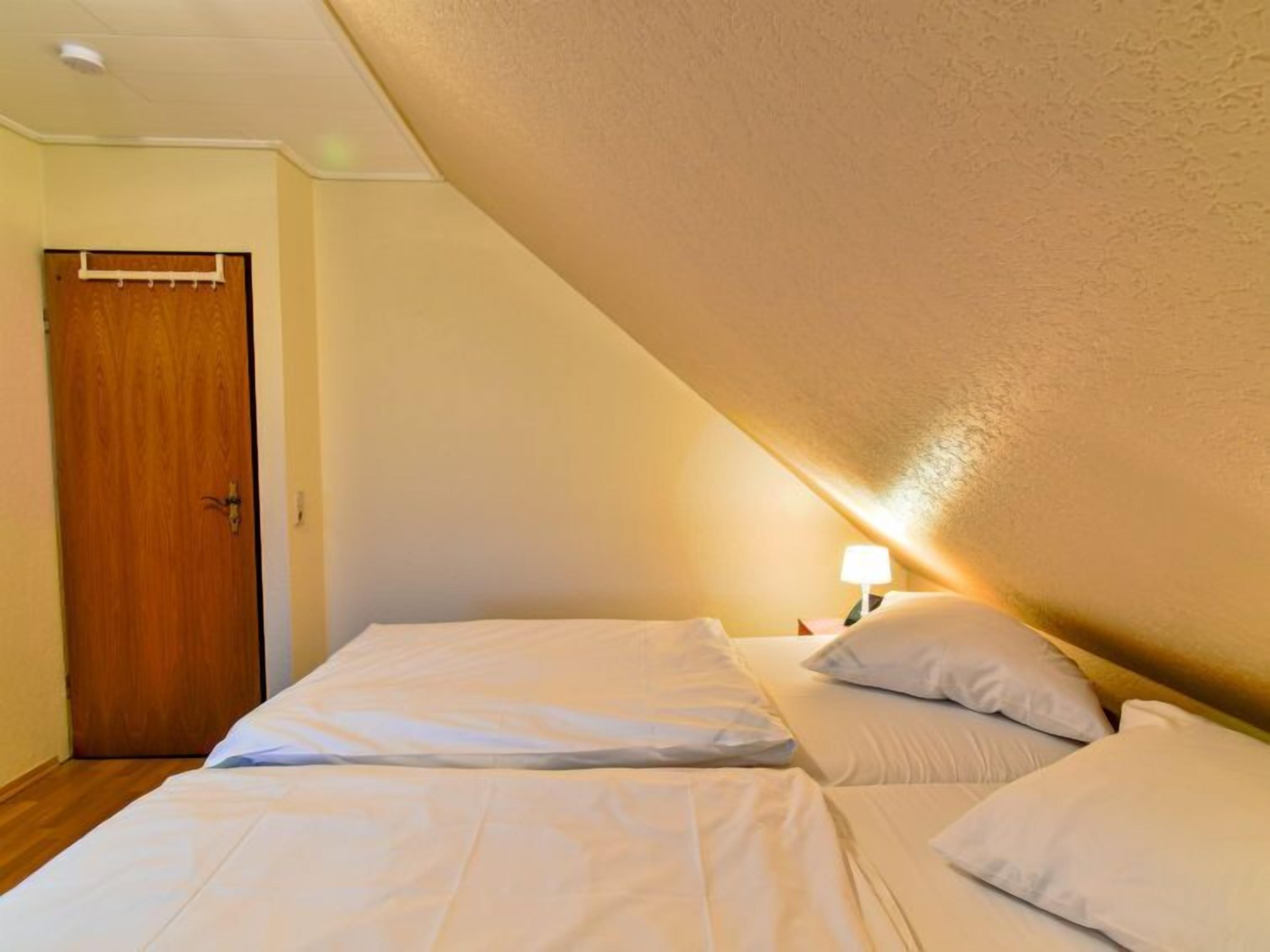 A bedroom with two beds, a wooden door, and a nightstand with a lamp.