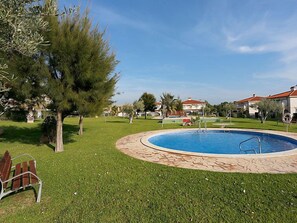 A swimming pool surrounded by a stone deck, with a grassy area and trees in the background.