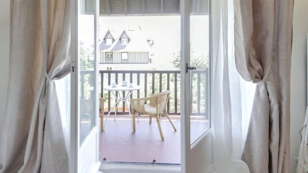 Een kamer met een schuifglasdeur die leidt naar een balkon met een tafel en stoelen.