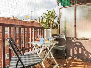 Une petite terrasse extérieure avec une table et deux chaises, un pot de fleurs et une vue sur un bâtiment en briques.