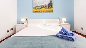 Ein Hotelzimmer mit einem Bett, zwei Nachttischen mit Lampen, einem Bild an der Wand und einem gefalteten Handtuch auf dem Bett.