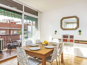Un coin repas avec une table en bois, des chaises blanches et une grande fenêtre.