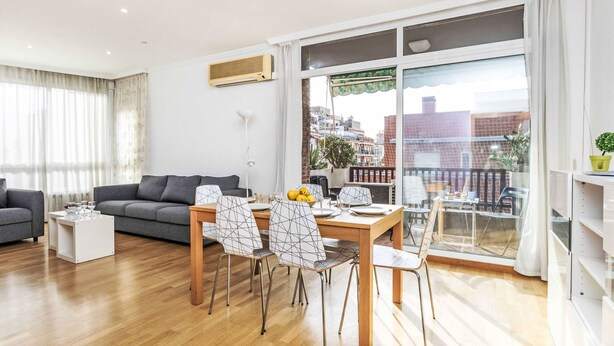 Ein modernes Wohnzimmer mit grauem Sofa, einem Esstisch mit Stühlen und einem großen Fenster mit Blick auf die Stadt.