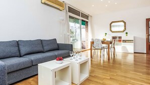 Ein modernes Wohnzimmer mit grauem Sofa, einem weißen Couchtisch und einem Essbereich mit Holztisch und Stühlen.