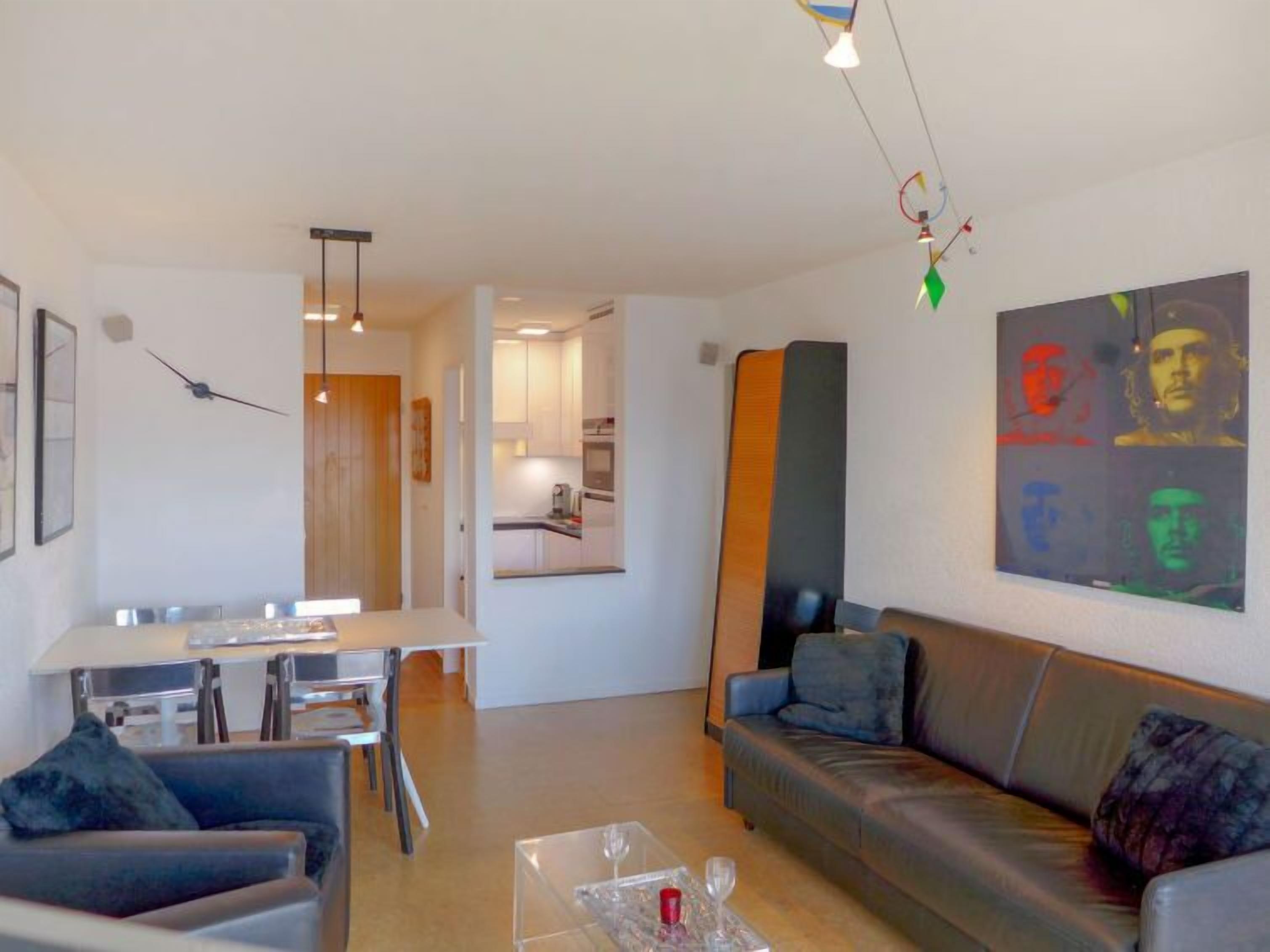 Ein modernes Wohnzimmer mit einer Couch, einem Esstisch und einer Küche im Hintergrund.