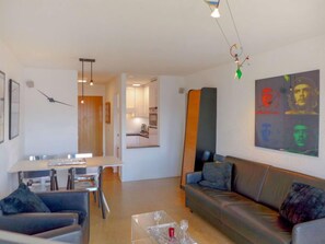 A modern living room with a sofa, a dining table, and a kitchen in the background.