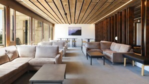 A modern lounge area with sofas and tables, large windows, and a wooden ceiling.