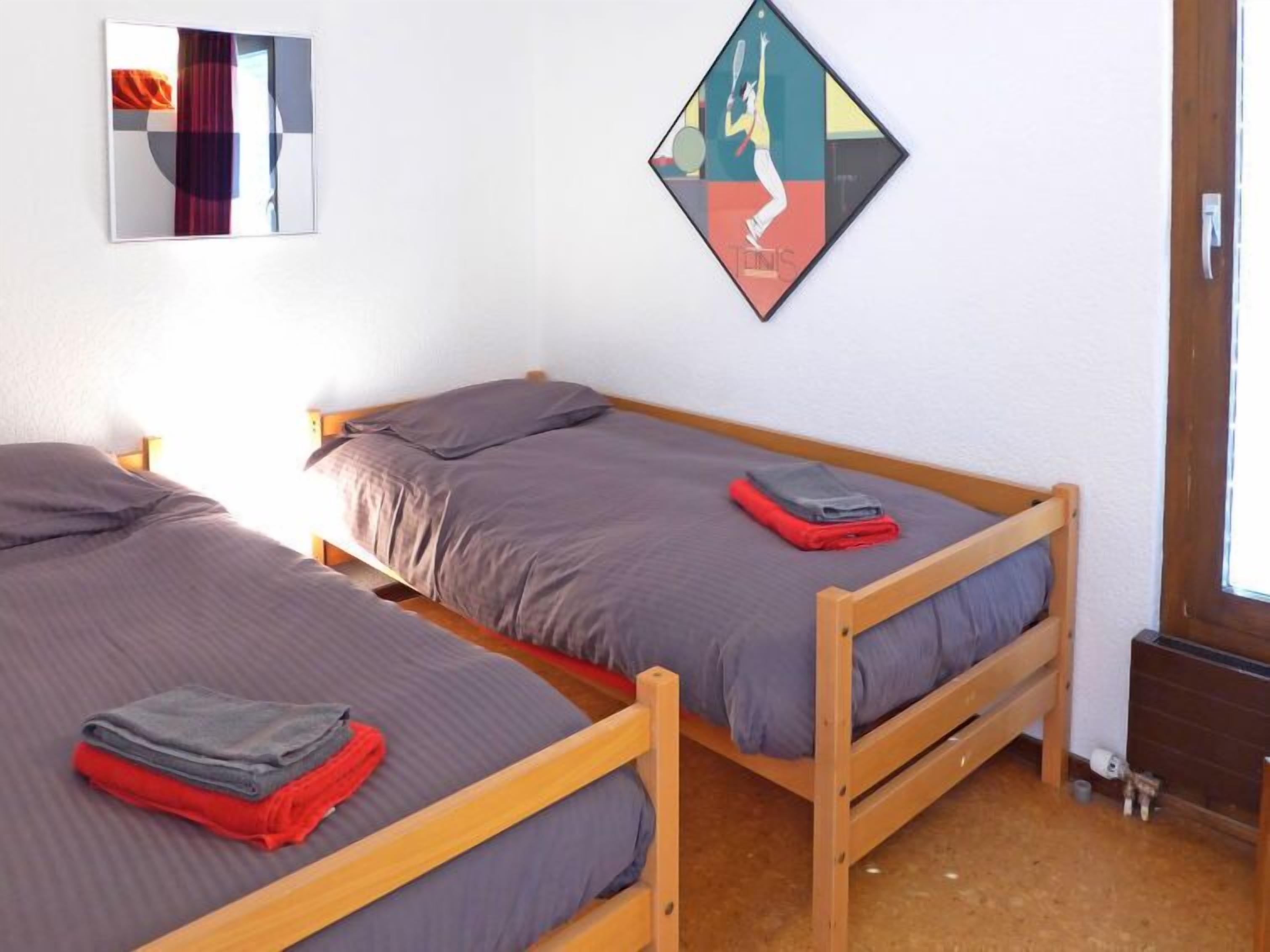 A room with two wooden beds, grey bedding, and a colorful abstract artwork on the wall.