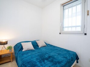 A bedroom with a bed, pillows, a bedside table with a lamp, and a window.
