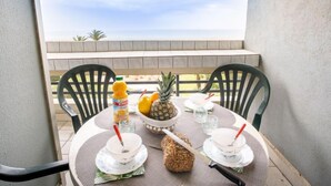 A balcony with a table set for two, featuring a pineapple, a loaf of bread, and a bottle of juice. - Le Beaupré by Interhome (Canet-Plage)