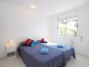 A bedroom with two beds, a nightstand, a window with a view, and a ceiling light.