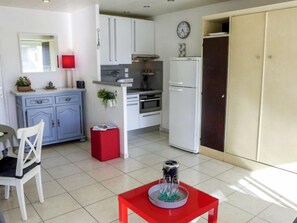 Een kleine keuken met witte kastjes, een rode tafel en een rode stoel.