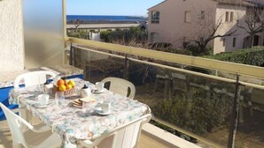 A balcony with a table set for breakfast, overlooking a coastal area with buildings and a clear sky. - De la Plage by Interhome (Cavalaire)
