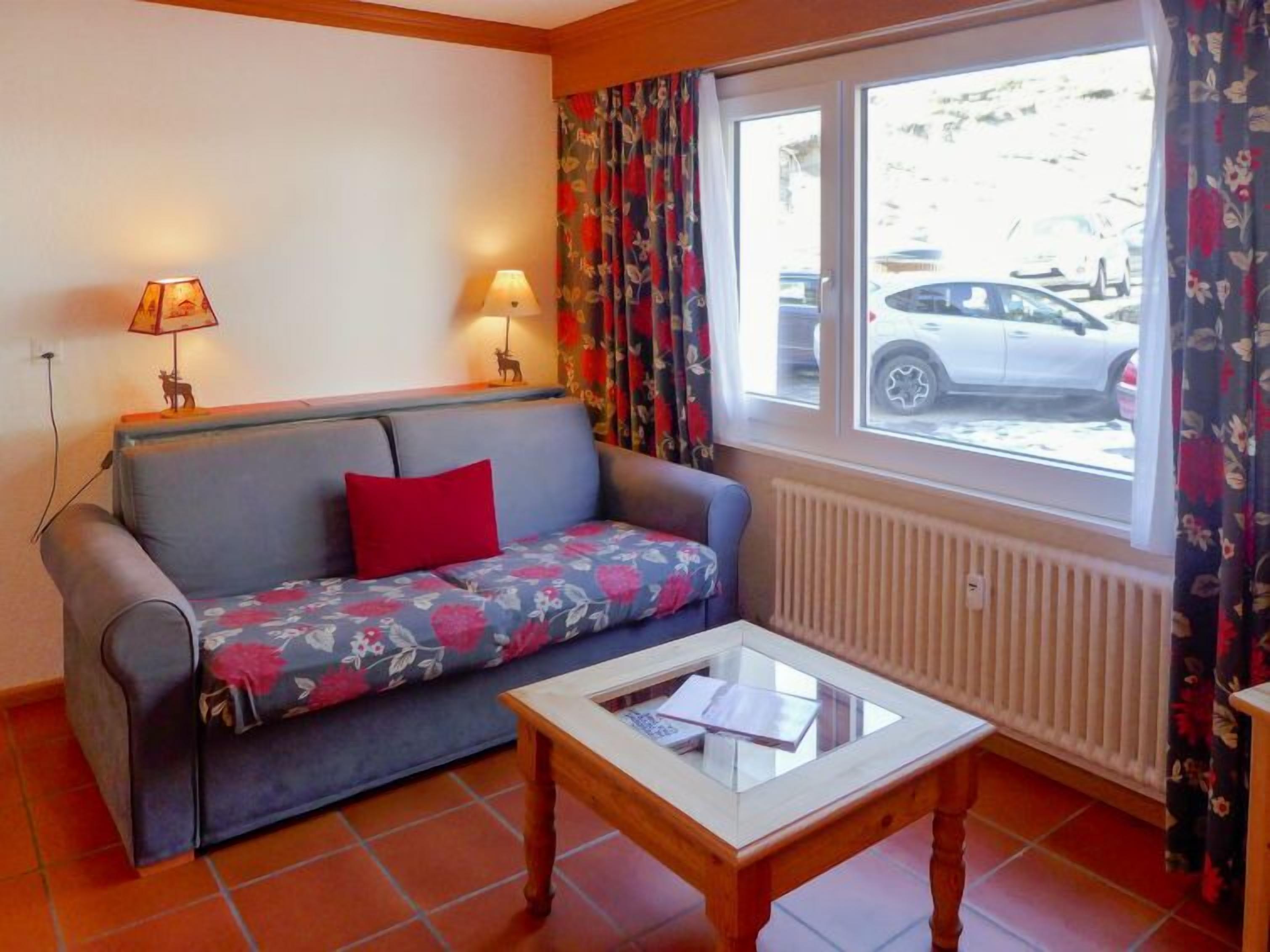 A room with a sofa, a small table, two lamps, and a window with curtains.