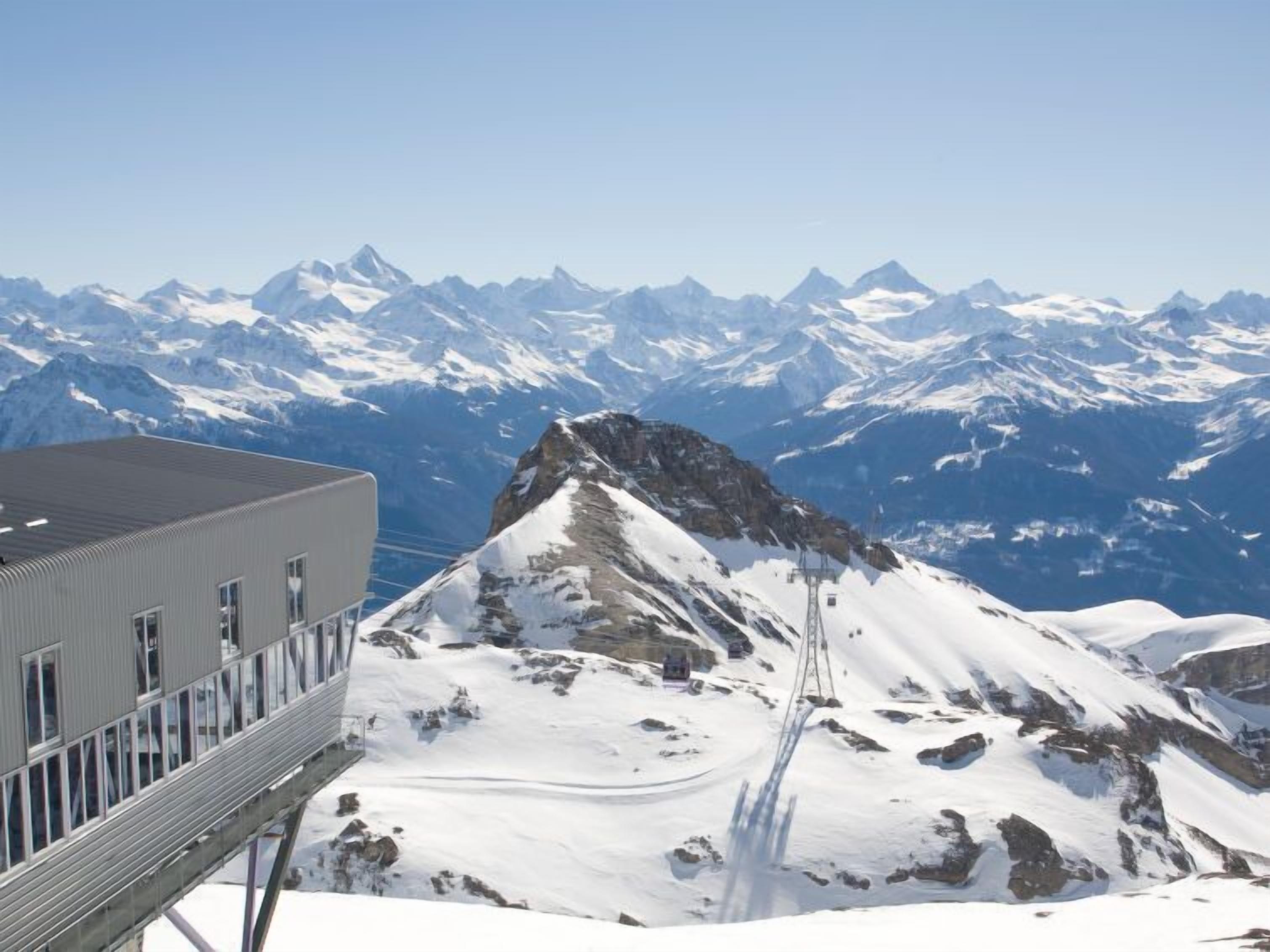 A mountain resort with a ski lift, snow-covered peaks, and a building with large windows.