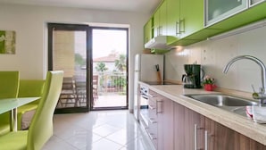 Eine moderne Küche mit grünen Schränken, ein Essbereich mit grünen Stühlen und eine Glastür, die auf einen Balkon führt.