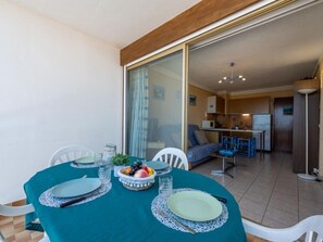 Un comedor con una mesa redonda preparada para cuatro, una cocina al fondo y un ventanal corredero que da a un espacio exterior.