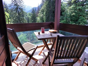 Eine Holzdiele mit Tisch und Stühlen, mit Blick auf eine bewaldete Berglandschaft.