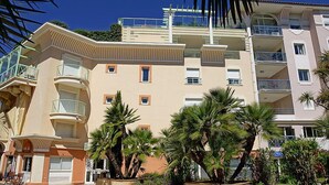 Un immeuble à plusieurs étages, doté de balcons, de palmiers et surplombant un ciel d’un bleu limpide.