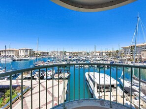 A marina with boats docked, a clear blue sky, and buildings in the background.