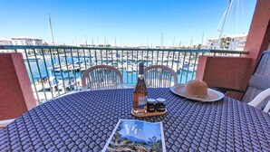 Une table avec un magazine, une bouteille et un chapeau, sur un balcon donnant sur une marina.