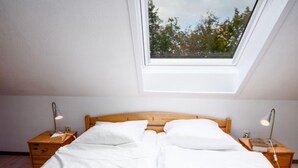 A bedroom with a skylight, a wooden bed frame, two bedside tables with lamps, and a view of trees through the window. - Muschelweg by Interhome (Norddeich)