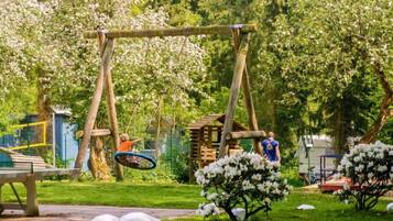 Ein Spielplatz mit Schaukel und Rutsche, umgeben von Bäumen und einem Picknicktisch.
