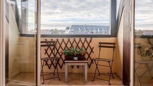 A balcony with a table and two chairs, a lattice wall, and a view of buildings. - Le Garden Fleuri by Interhome (Blonville sur mer)