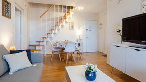 A modern living room with a staircase, a dining area, and a TV on a cabinet. - Le Garden Fleuri by Interhome (Blonville sur mer)