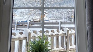 Ein Fenster mit Blick auf eine verschneite Landschaft, darunter kahl stehende Bäume und ein Holzzaun.