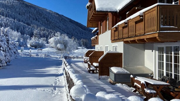 Eine Holzhütte mit einem mit Schnee bedeckten Balkon, einem Holzzaun und freiem Blick auf einen verschneiten Berg im Hintergrund.