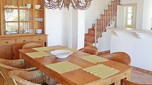 Zona pranzo con tavolo in legno, sedie in vimini, un lampadario e una scala.