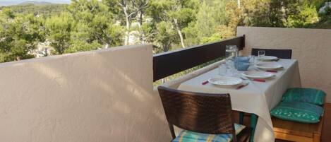 A terrace with a table set for dining, chairs, and a view of a forested landscape.