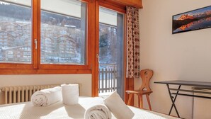 A room with a large window, a wooden chair, a small table, and rolled towels on the bed. - Ecluses 2 by Interhome (Nendaz)
