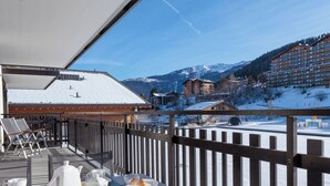 A balcony with a table set for breakfast, overlooking a snowy mountain landscape and a hotel building. - Ecluses 2 by Interhome (Nendaz)