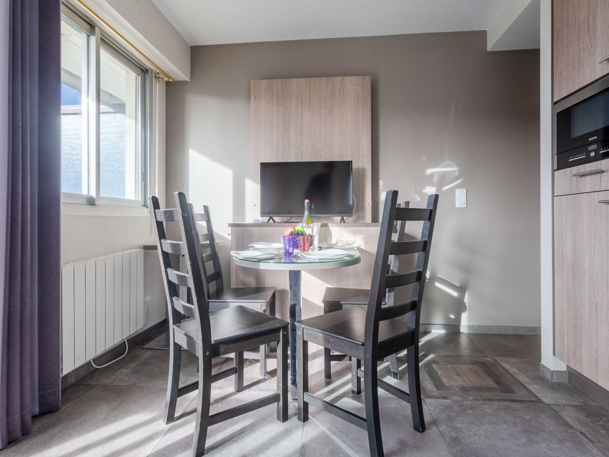 Een moderne keuken met een ingebouwde oven, een eettafel met vier stoelen en een flatscreen televisie aan de muur.
