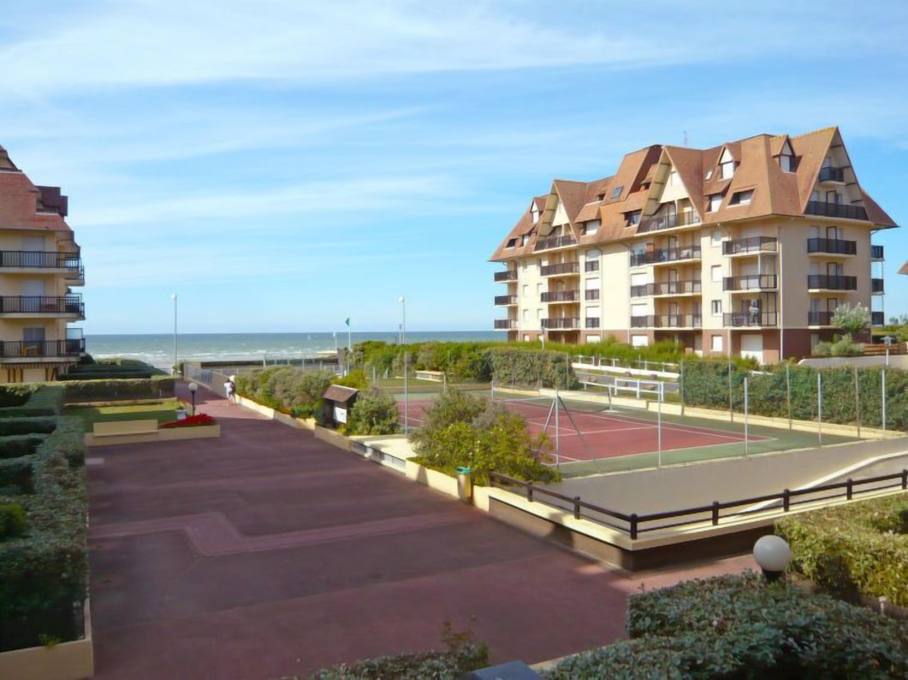 Um edifício residencial com várias varandas, quadra de tênis e vista para o mar.