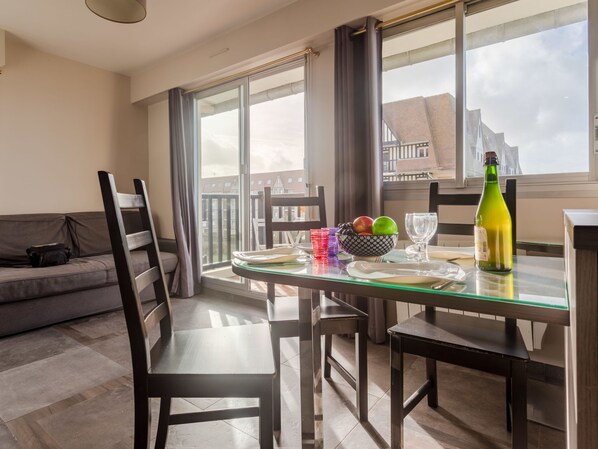 A dining area with a glass table, chairs, a bottle of wine, and a bowl of fruit.