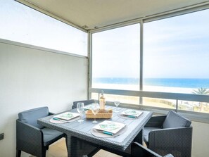 A balcony with a table set for four, overlooking a beach.
