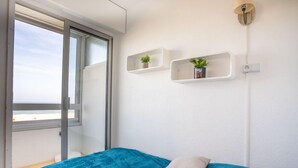 Un dormitori amb un llit, una finestra i dues baldas penjades a la paret amb plantes.